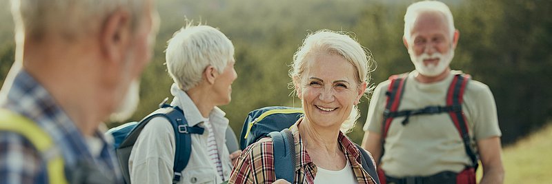 Ältere Menschen wandern in den Bergen, lachen und genießen die Natur und die frische Luft.