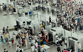 Reisende in einem Flughafen-Terminal, die auf ihre Flüge warten und sich zwischen den Gates und Geschäften bewegen.